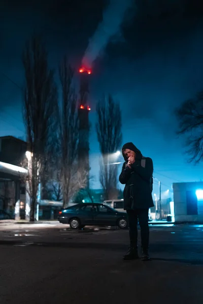 Jeune homme porter manteau avec capuche la nuit dans la ville colorée au néon fume cigarette Photos De Stock Libres De Droits