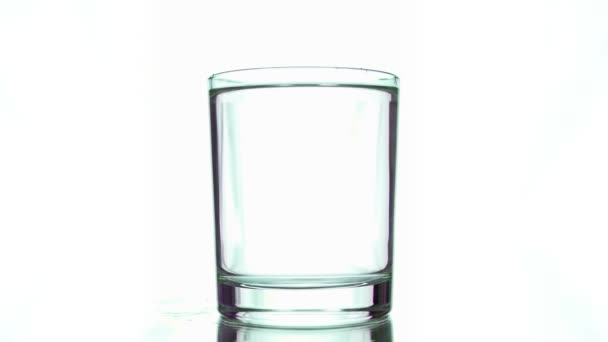 En un vaso de agua transparente sobre un fondo blanco caen varias tintas verdes — Vídeo de stock