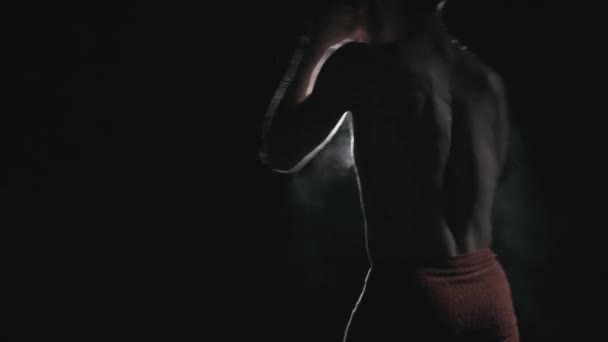 En ung bokser træner hårdt i mørke modsat et lys – Stock-video