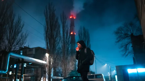 Shoot of a smoking modern man in hooded coat with industrial zone on background Obraz Stockowy