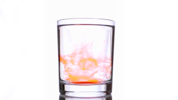 Déplacement de peinture orange liquide tombant dans un verre d'eau sur fond blanc — Video