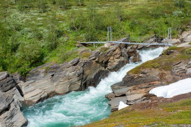 İsveç 'in Lapland kentindeki Padjelanta milli parkındaki hızlı akan çalkantılı nehir üzerinde dağlardaki asma köprü..