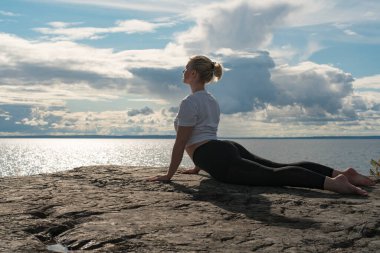 Yoga yapan, meditasyon yapan ya da Cliff 'in üzerinde suya yakın esneyerek güzel manzarada farklı pozlar veren bir kadın. İdeal sakin meditasyon yeri bulma kavramı, kendinizi ve sağlıklı yaşamı bulma kavramı.