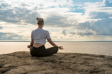 Yoga yapan, meditasyon yapan ya da Cliff 'in üzerinde suya yakın esneyerek güzel manzarada farklı pozlar veren bir kadın. İdeal sakin meditasyon yeri bulma kavramı, kendinizi ve sağlıklı yaşamı bulma kavramı.