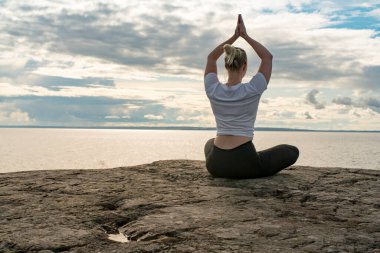 Yoga yapan, meditasyon yapan ya da Cliff 'in üzerinde suya yakın esneyerek güzel manzarada farklı pozlar veren bir kadın. İdeal sakin meditasyon yeri bulma kavramı, kendinizi ve sağlıklı yaşamı bulma kavramı.