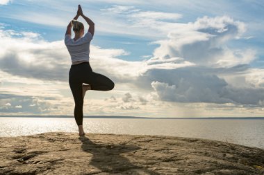 Yoga yapan, meditasyon yapan ya da Cliff 'in üzerinde suya yakın esneyerek güzel manzarada farklı pozlar veren bir kadın. İdeal sakin meditasyon yeri bulma kavramı, kendinizi ve sağlıklı yaşamı bulma kavramı.