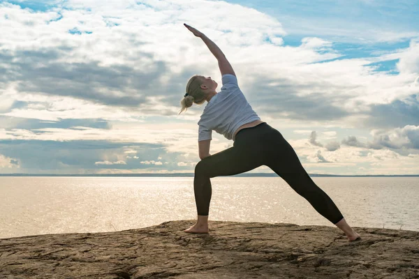 Woman practicing Yoga, meditation or stretching close to water on Cliff doing different poses on beautiful landscape. Concept of finding ideal calm meditation place, finding yourself and Healthy Life.