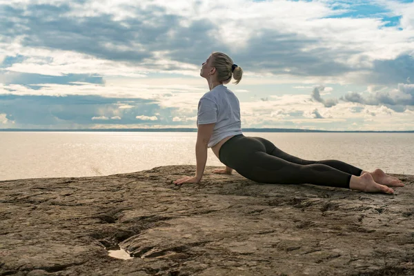 Woman practicing Yoga, meditation or stretching close to water on Cliff doing different poses on beautiful landscape. Concept of finding ideal calm meditation place, finding yourself and Healthy Life.