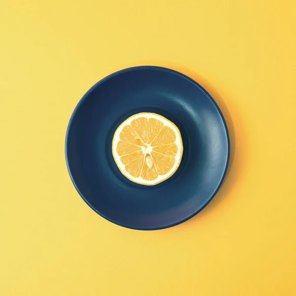 A slice of summer lemon fruit on a plate in a minimalist concept with a square background.