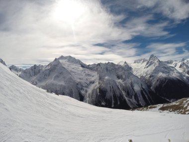 Güneşli bir günde karlı dağların manzarası. Mavi gökyüzü bulutlarla kaplı.