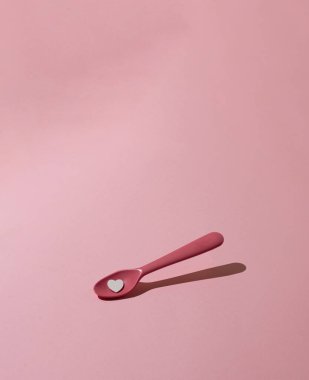 Pembe, pembe pastel arka planda kalbi olan plastik bir kaşık. Yaratıcı, asgari konsept.