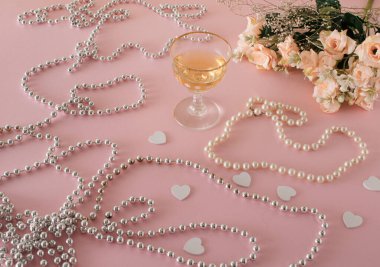 Güller, beyaz kalpler, parlak inciler ve bir bardak içecekle romantik bir kompozisyon. Pastel pembe konsept.