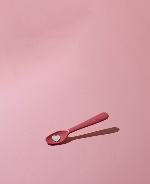 Розовая, пластиковая ложка с сердцем на розовом пастельном фоне. Творческая, минимальная концепция.