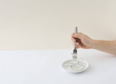 Müzik bağımlısı. Çatalla el, makarna yerine kulaklık. Minimum konsept. Beyaz bej arkaplan.