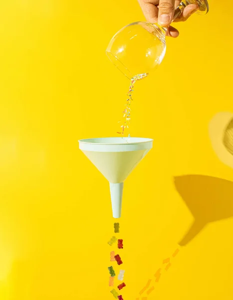 colorful candies falling from glass thru funnel and fall like gummy bears on other side. creative colorful concept. bright yellow background.