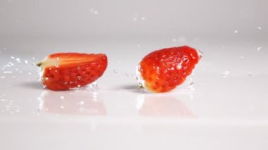 Sliced strawberry drop on white surface