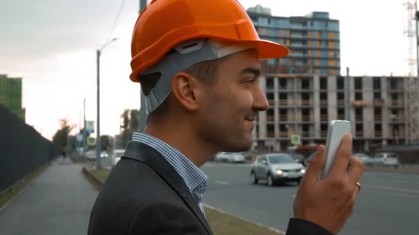 Construtor em um capacete laranja está fazendo chamada — Vídeo de Stock
