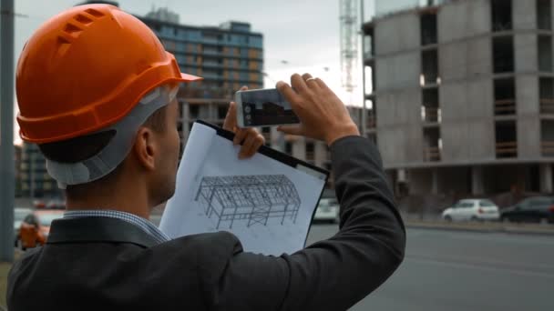 Інженер зі смартфоном фотографує будівництво — стокове відео