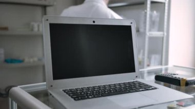 Eczanedeki dizüstü bilgisayar ekranı arka planda eczacıyla izlenmeye hazır.
