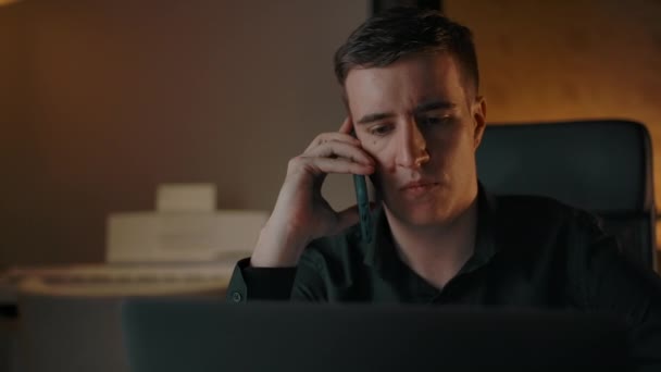 A young entrepreneur behind a laptop answers the phone — Stock Video