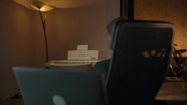 Adam sandalyesinde döner ve dizüstü bilgisayarın klavyesine yazmaya başlar.