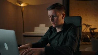 Bir adam dizüstü bilgisayara klavye yazar ve ev içi bir çağrıya cevap verir..