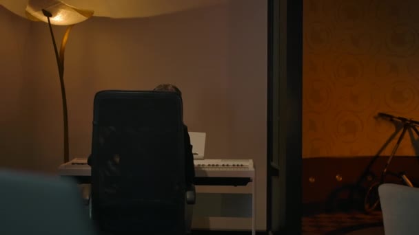 Молодой композитор играет на фортепиано и идет к ноутбуку для записи — стоковое видео