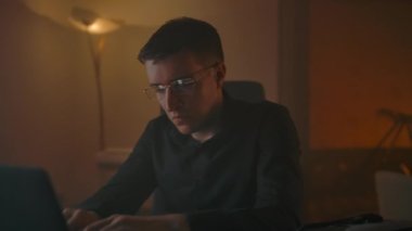 Bir adam dizüstü bilgisayarın önünde çalışırken gözlüklerini çıkarır ve göz masajı yapar.