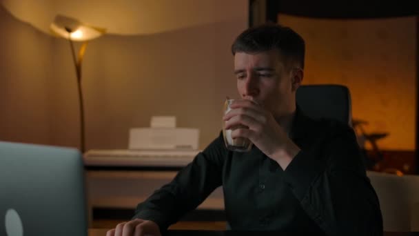 Bărbatul caucazian bea cafea acasă seara uitându-se la laptop — Videoclip de stoc