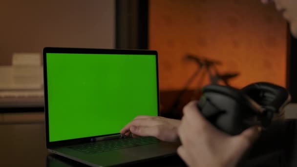 Человек в шлеме виртуальной реальности, печатающий на клавиатуре ноутбука с зеленым экраном — стоковое видео