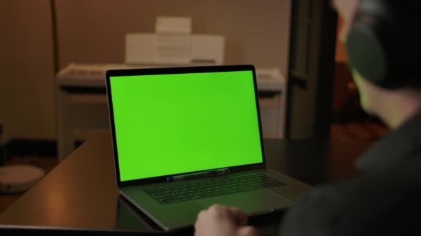Blanke man in hoofdtelefoon luisteren muziek achter groene scherm laptop. — Stockvideo