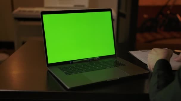 Ein Mann macht sich Notizen, lernt online auf einem Laptop mit grünem Bildschirm — Stockvideo