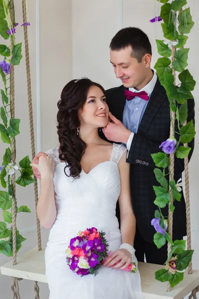 Groom hugs bride sitting on a swing with the vine — Stock Photo, Image