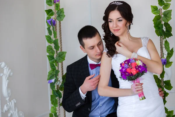 Bridegroom is sitting on a swing and caresses the bride — Stock Photo, Image