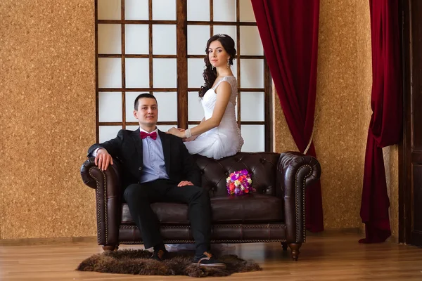 Bride and groom sitting on a leather sofa in the loft — Stock Photo, Image