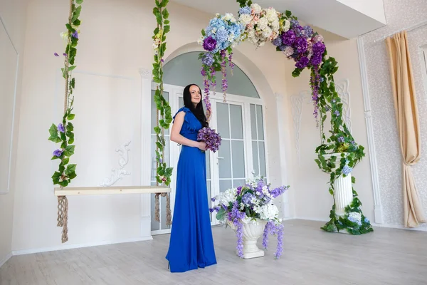 Ragazza in abito blu vicino alle altalene e archi di fiori — Foto Stock