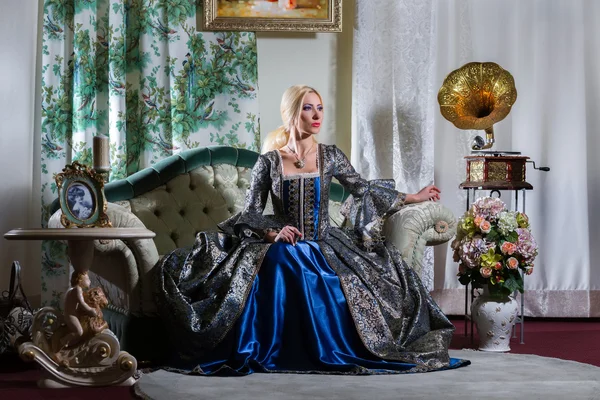 Woman in medieval dress sits on a sofa — Stock Photo, Image