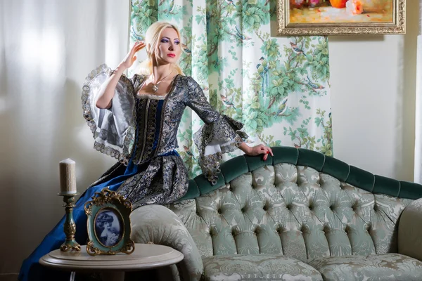 Girl in medieval dress sits on a sofa — Stock Photo, Image