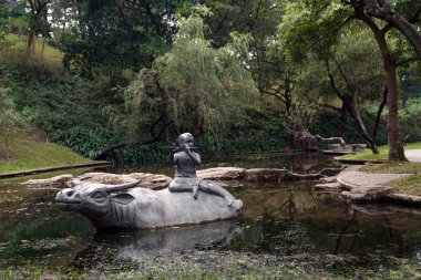 Bir çocuk heykeli flüt çalıyor, parkta bir bufalonun üzerinde oturuyor.