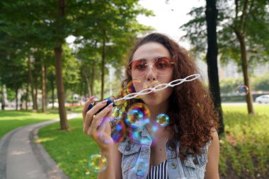 Bir kız parkta sabun köpüğü üflüyor.