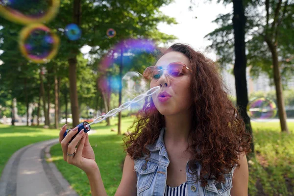 Bir kız parkta sabun köpüğü üflüyor.