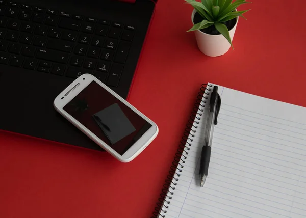 Üst manzara masası. Not defteri ve akıllı telefonu olan Kırmızı Arkaplan ofis masası