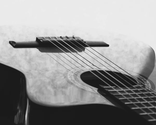 Gitarın telleri, boynu, perdeleri, çantası, köprüsü gibi farklı kısımları olan klasik bir akustik gitarın yakın çekimi. Siyah beyaz fotoğraf.