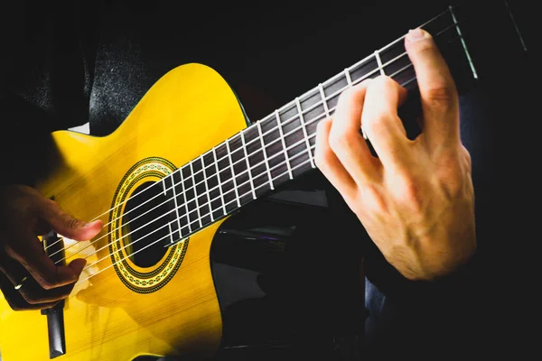Akustik gitar çalan bir adamın elleri. Klasik gitarın farklı parçaları, vücut, teller, boyun, perdeler gibi. Siyah arkaplan