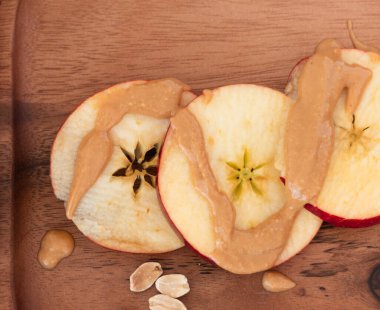 Ahşap tabakta fıstık ezmeli elma dilimlerinin üst görüntüsü.