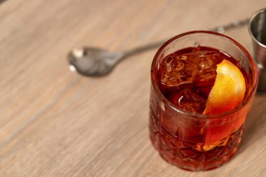 Negroni kokteylinin ahşap yüzeyde turuncu kaşık ile karıştırılmış görüntüsü.