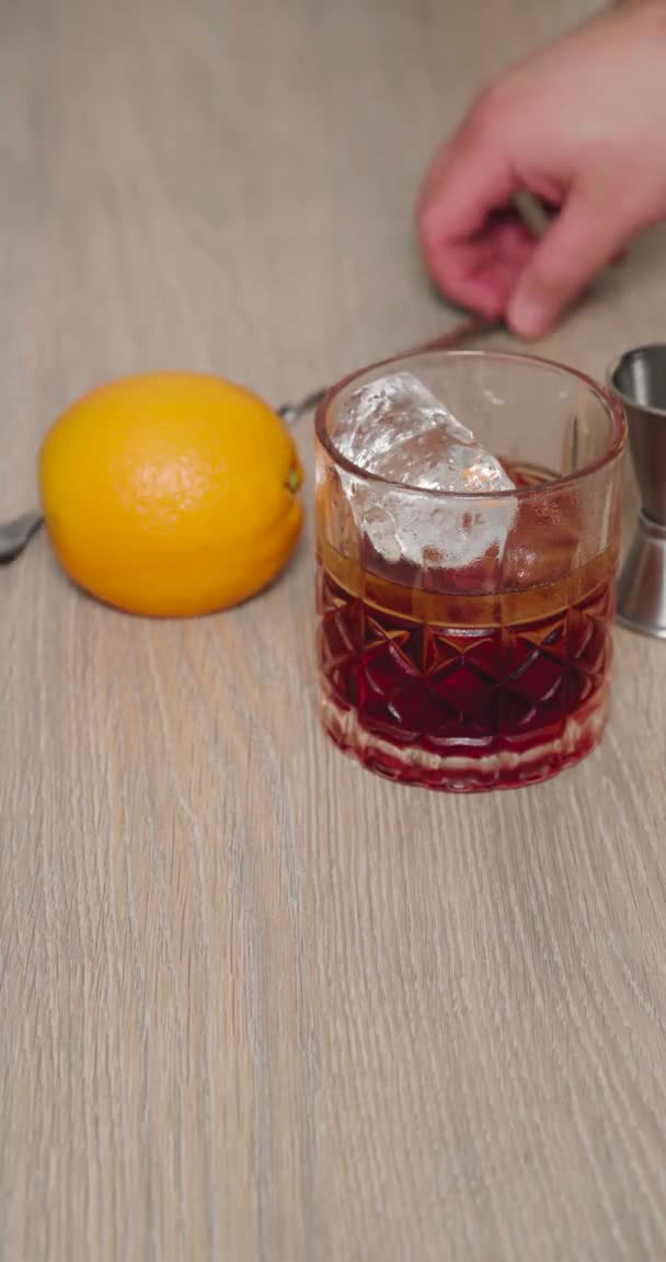 片手でスプーンを持ってかき混ぜている間に氷とネグローニの完全なガラス — ストック動画