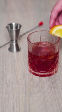 Negroni ile buz dolu bir bardağın kenarına taze turuncu bir parçanın içi ile dokunurken yavaşça hareket etmesi..