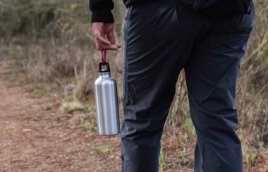Su dolu gümüş bir termos şişesi taşıyan bir elin yakından görüntüsü..