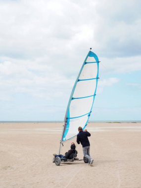 Fransa 'da Plage de Ouistreham plajında yelken açan bir deniz yatı. Bir adam kumsalda bir yata yardım ediyor.